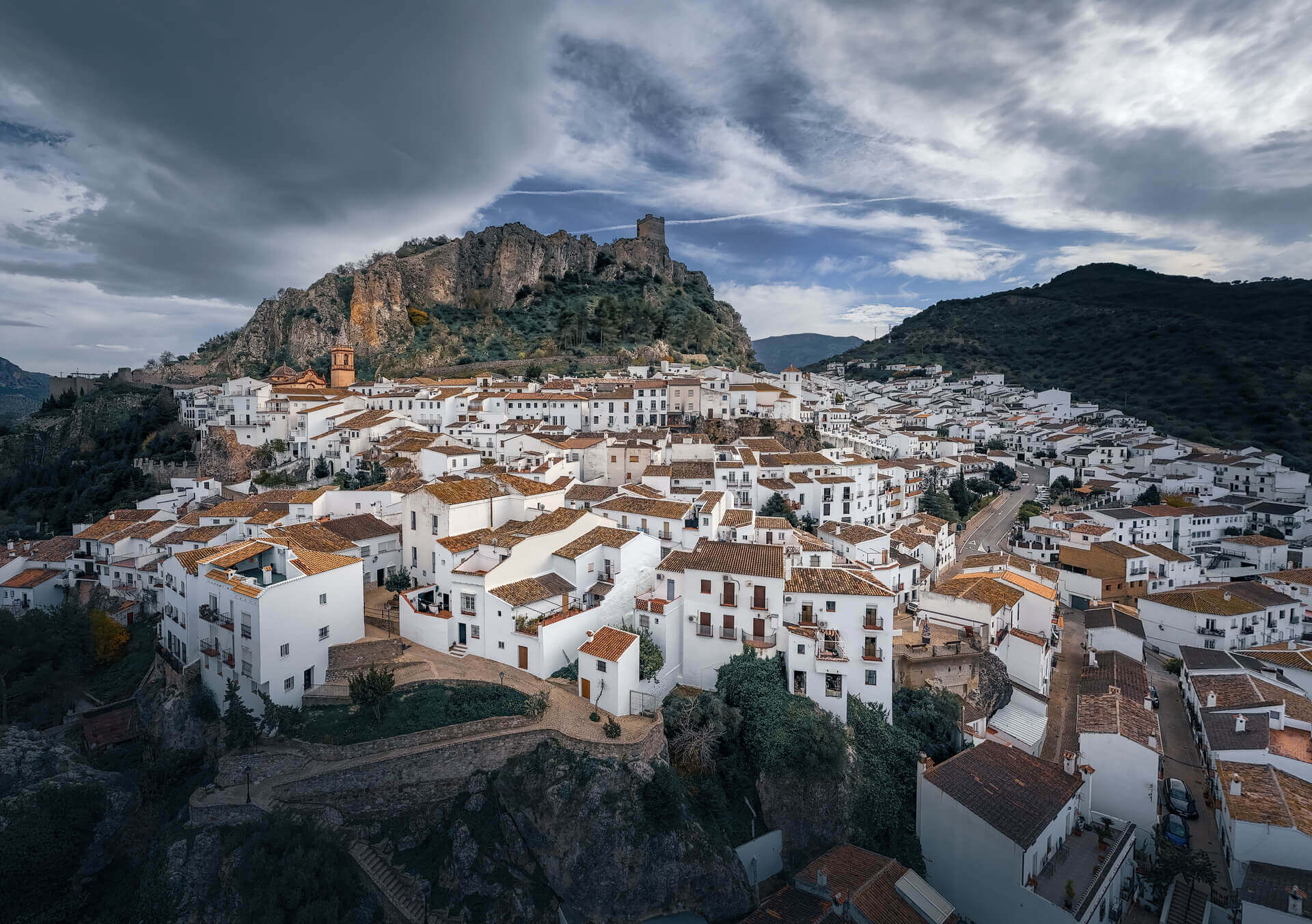Old white villa on the hillside beneath a cloudy sky on a sunny day in Zahara de la Sierra, Andalusia, Spain